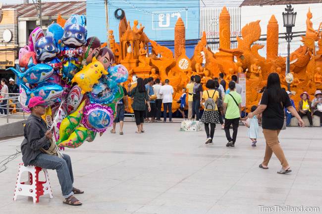 man selling balloons next to Khao Phansa candle parade float