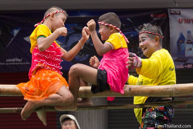 two kids boxing while balanced on a bamboo pole in Khao Phansa candle parade