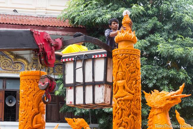 two men in a crane putting the top on a Khao Phansa candle parade float