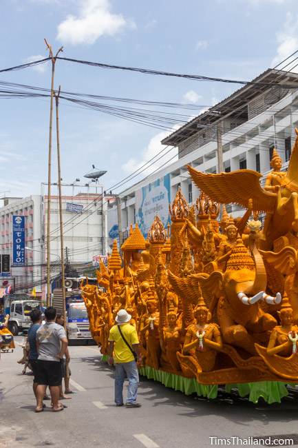 men lifting power lines over a Khao Phansa candle parade float driving down the street