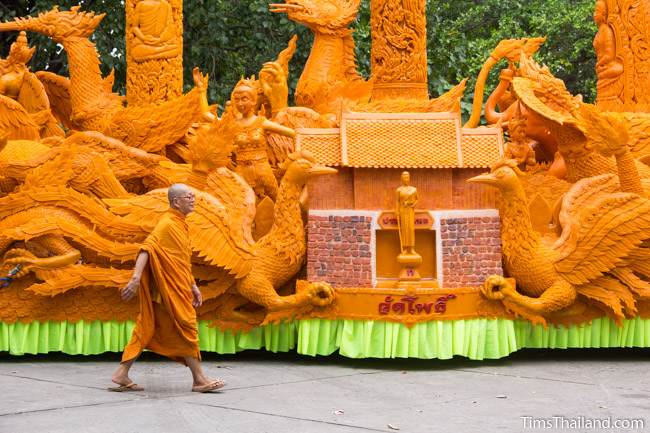 monk walking on front of a Khao Phansa candle parade float with the Thao Suranari Monument and Chumphon Gate on it