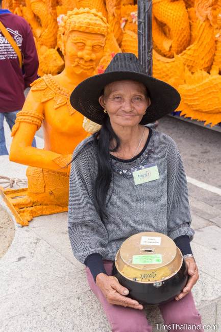 woman collecting donations for her temple in front of a Khao Phansa candle parade float