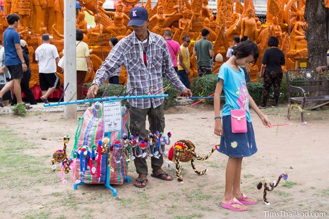 man selling puppets in front of a Khao Phansa candle parade float
