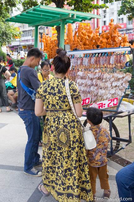 man selling dried squid in front of a Khao Phansa candle parade float