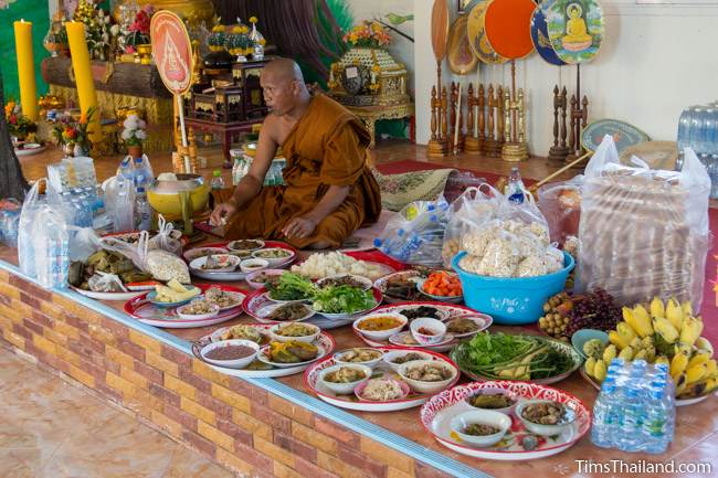 monk eating with many food trays next to him