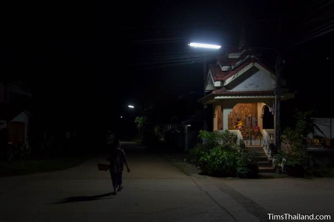 woman walking through village at night during Boon Khao Pradap Din