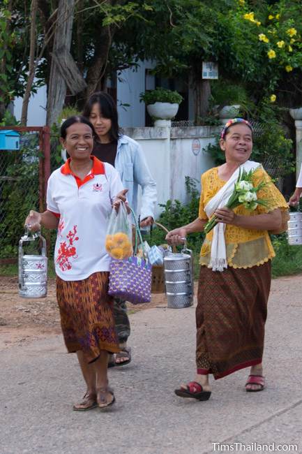women walking through village in morning during Boon Khao Pradap Din