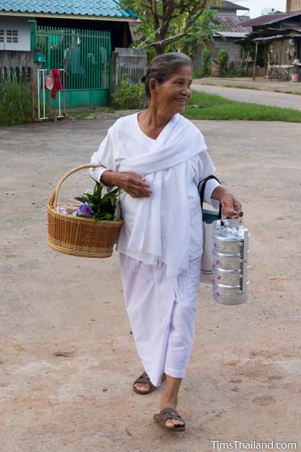 woman wearing white walking through village in morning during Boon Khao Pradap Din
