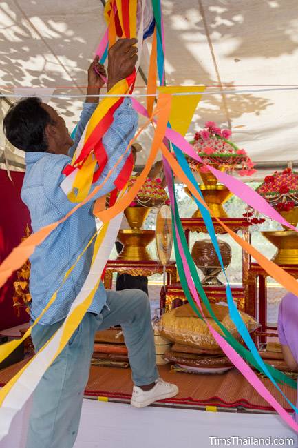 man hanging streamers to decorate tent for Kathin celebration