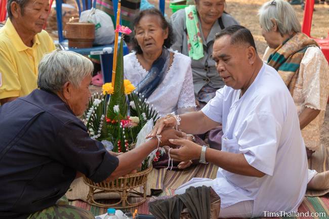 man tying sai sin sacred thread on man's wrist at Boon Berk Bahn