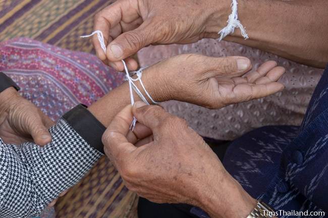 man tying sai sin sacred thread on man's wrist at Boon Berk Bahn