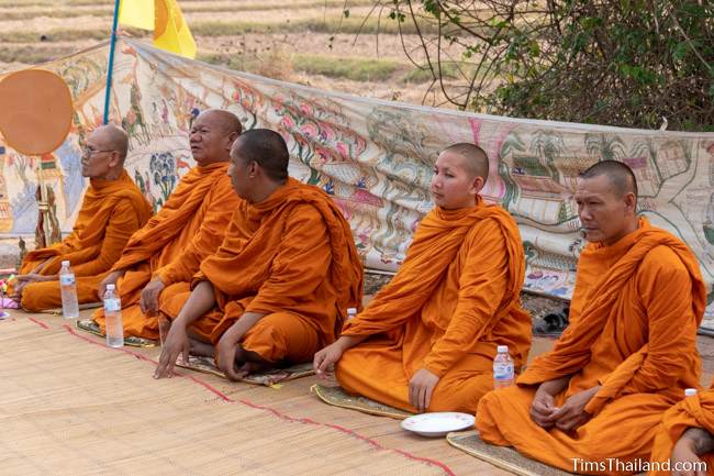 monks sitting in front of Pha Wet banner