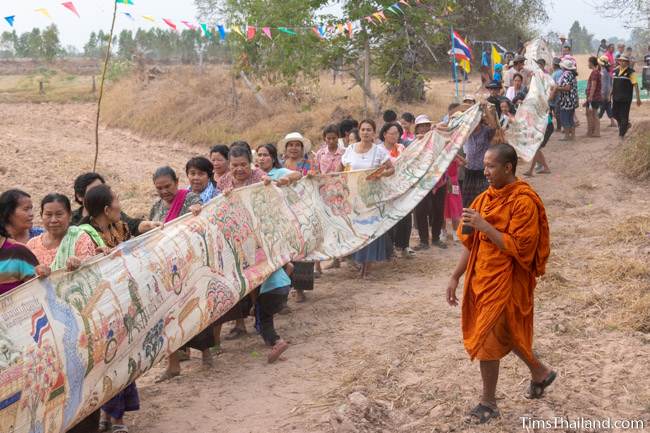 people carrying Pha Wet banner through a rice field