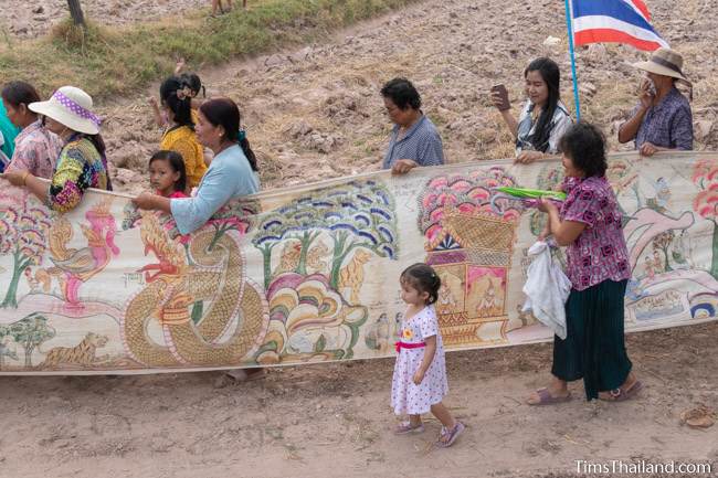 people carrying Pha Wet banner through a rice field