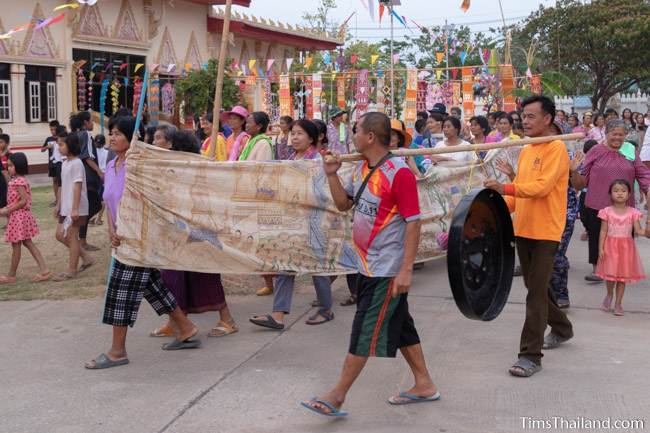 people carrying Pha Wet banner and gong at temple
