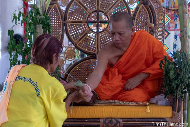 woman tying sacred thread aroudn monk's wrist