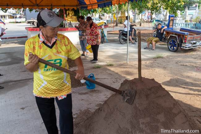 patting down sand with a hoe on a sand stupa