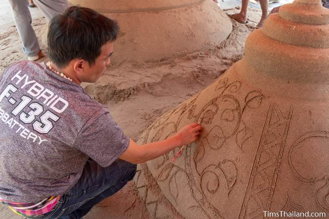 man carving design into sand stupa