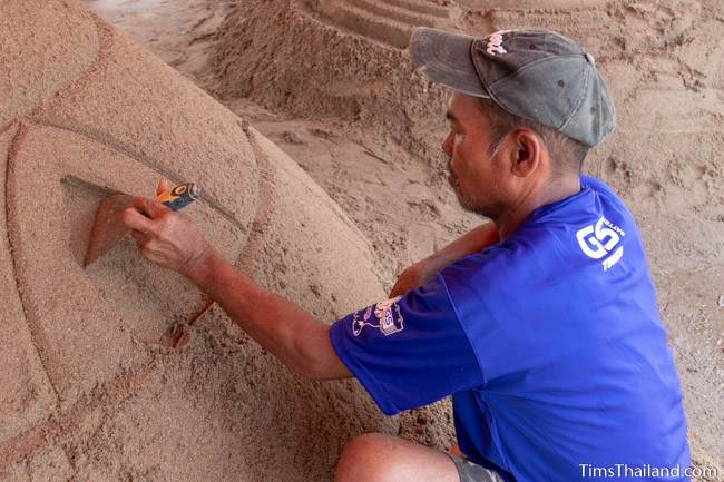 man carving design into sand stupa