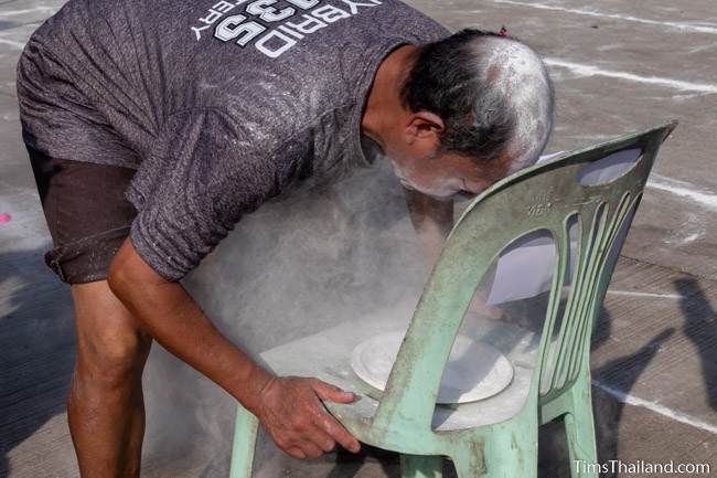 man blowing powder to find a coin