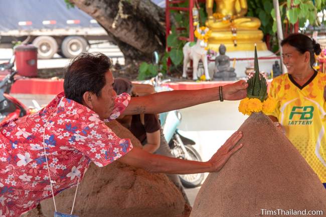 man putting flowers atop a sand stupa