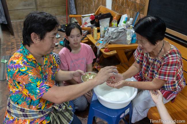 man pouring water over hands of an old woman