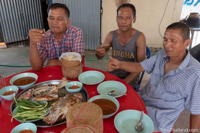 men at a table eating grilled fish with sticky rice