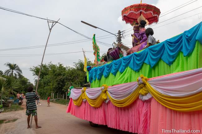 man with bamboo pole lifting power line to let parade float pass under