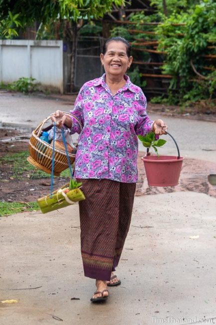 woman carrying kratong, food basket, and water bucket