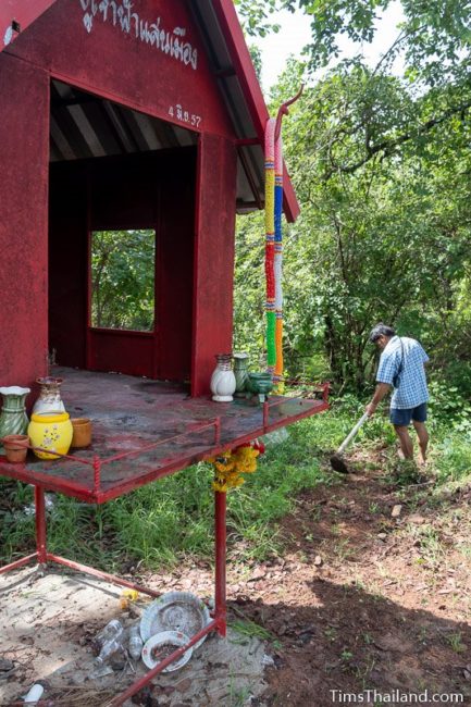 man with hoe clearing ground next to shrine