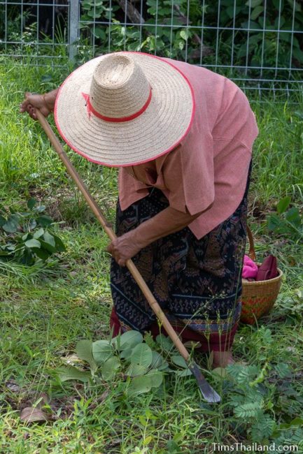 woman with hoe clearing ground next to shrine