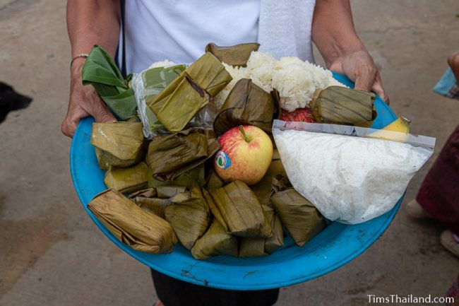 woman holding tray of fruit, rice, and snacks in banana leaves