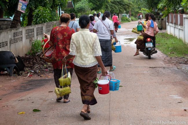 women walking home with kratong and water buckets after ceremony
