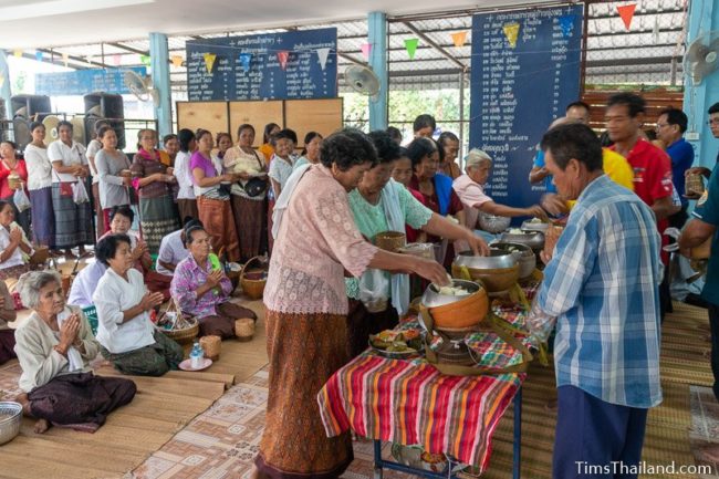 people putting food in monk alms bowls