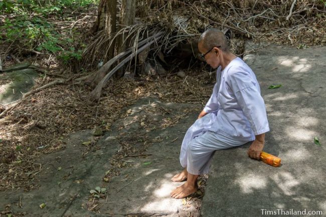 Buddhist nun sitting on long sandstone cutting edge in bedrock