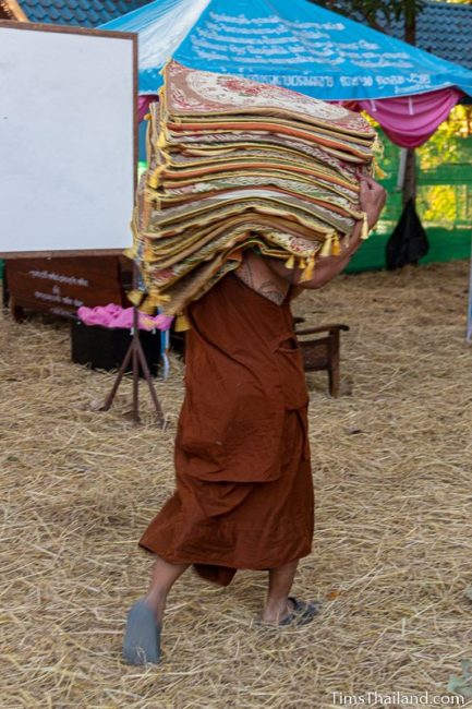 monk carrying a pile of meditation mats