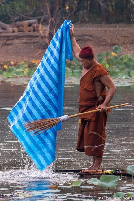 man washing a plastic mat in a pond