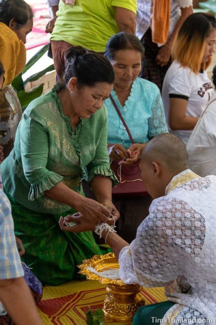 tying string around wrist of a man who will become a monk