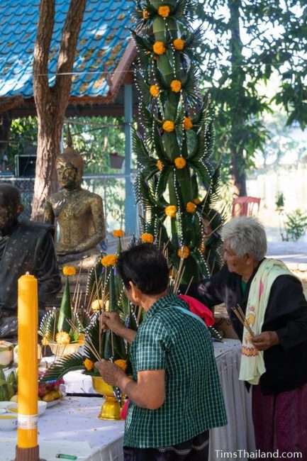 people lighting incense around a monk statue