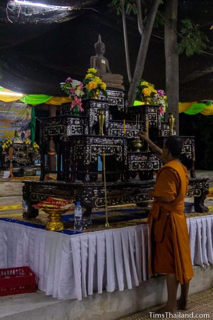 monk lighting incense in front of Buddha image