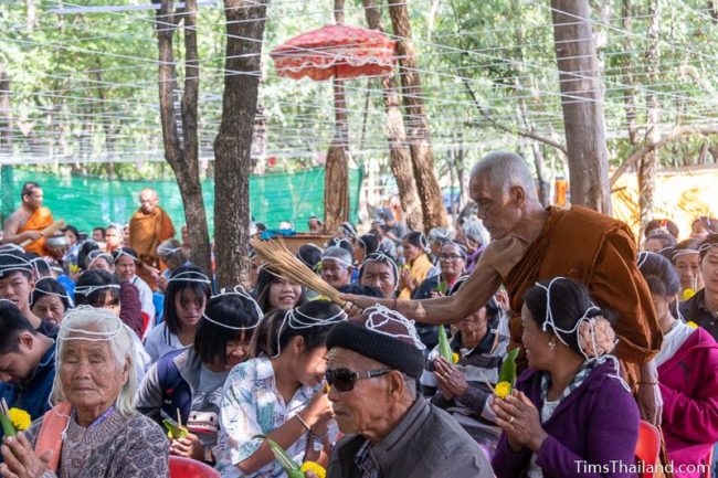 monk splashing water on people who have strings on their heads