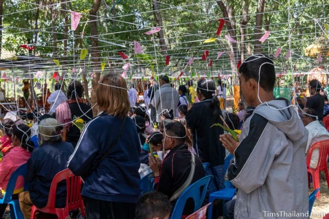 people with white string tied above them standing and praying