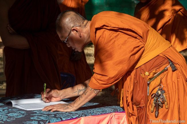 monk signing his name in a notebook