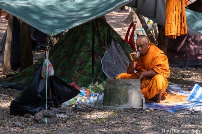 man drinking coffee next to his tent