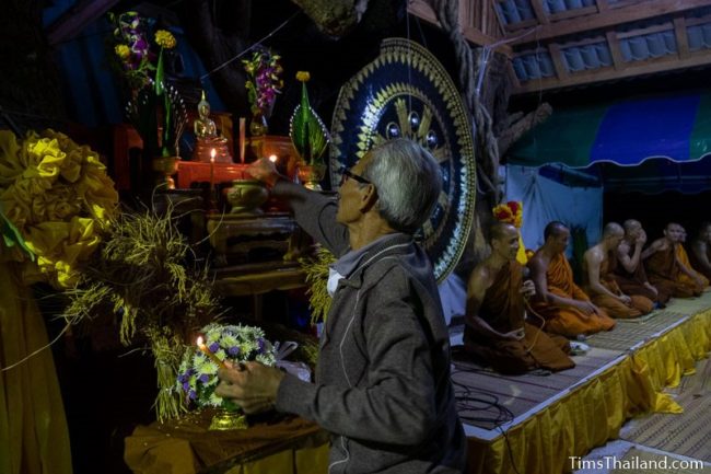 man lighting candles in front of a Buddha image