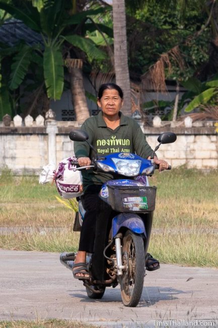 woman bringing rice to the temple on back of a motorcycle