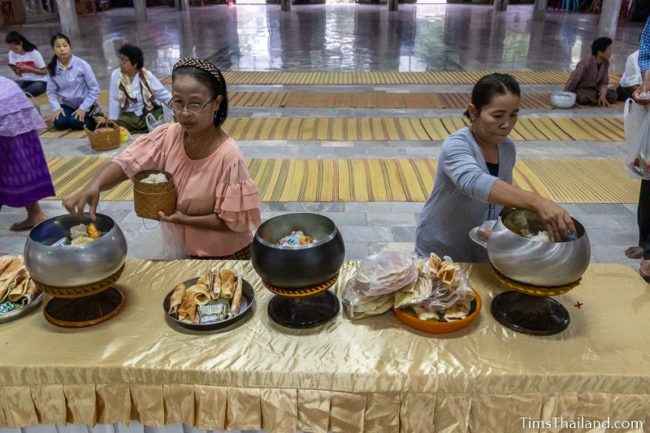 women putting food in monk alms bowls