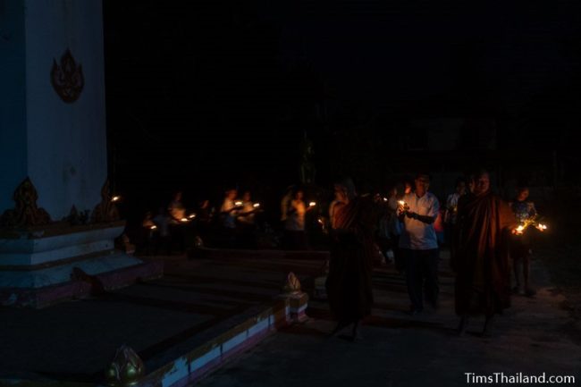 people holding candles walking around a stupa