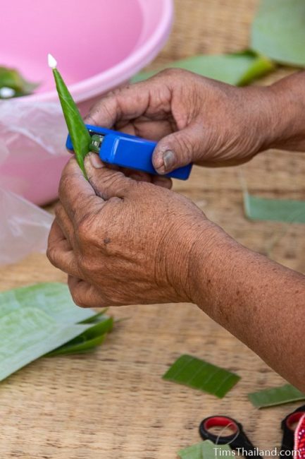 closeup of woman stapling banana leaf to make bai sii