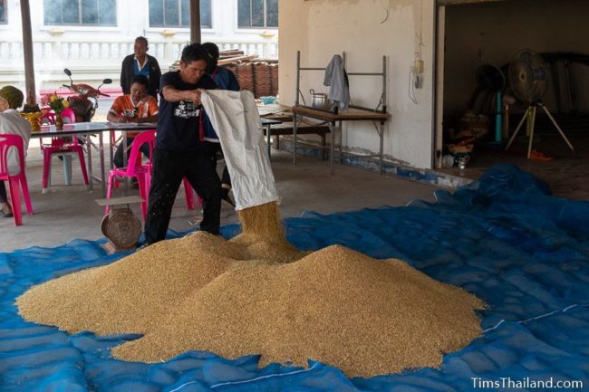 man pouring rice from a bag onto the big pile